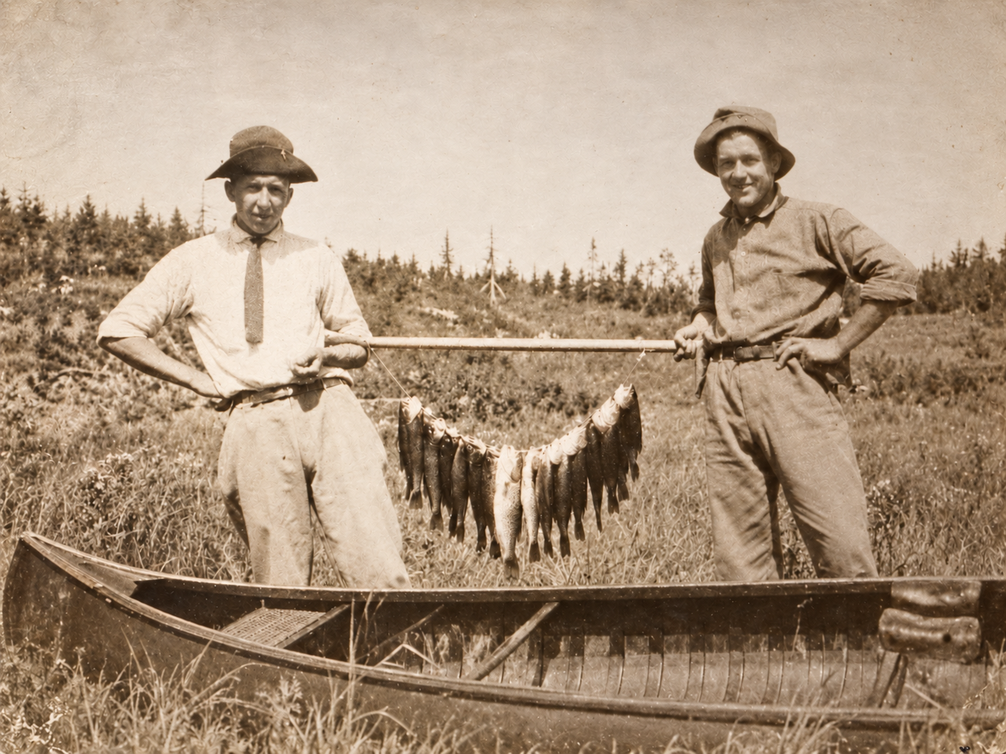 Two men pose beside a canoe with a string of fish during a family canoe-and-fishing outing.