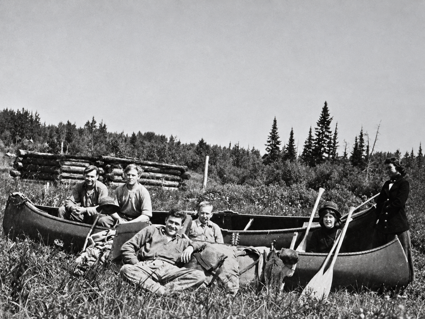 Family group with three canoes and a dog beside a log camp, circa 1930s to 1940s.